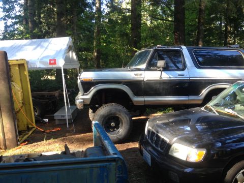 1971 Ford F-250 - A lifted 1978 Ford Bronco is parked next to a black SUV in a wooded area.