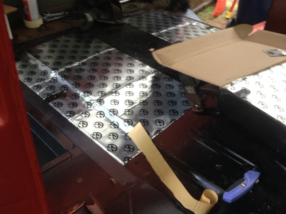 Installing sound deadening material on the floor of a vehicle interior. Cardboard box is open on the right