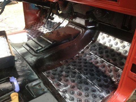 1971 Ford F-250 - Stripped red truck cab floor showing the transmission tunnel and shiny dimpled sound-deadening mat being installed.