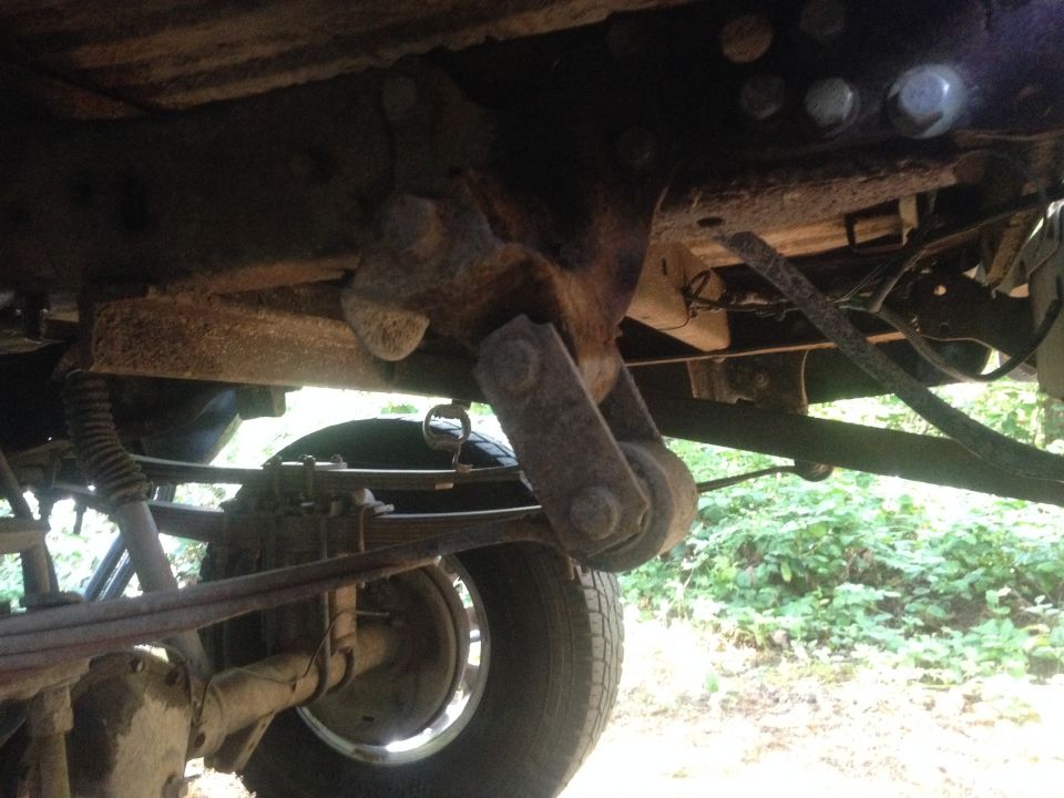 Underside view of a truck's suspension and leaf springs. Shows rust and wear on components