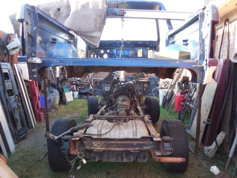 1993 Ford Bronco - Body-off shot in a backyard: a blue truck/SUV body shell is held up on jack stands and steel posts while the bare rolling frame sits beneat…