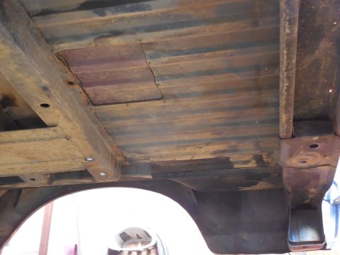 1993 Ford Bronco - Underside view of a ribbed steel cargo floor pan on a body lifted off its frame, showing heavy surface rust, a welded-in rectangular patch…
