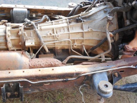 1993 Ford Bronco - Underside view of a truck's frame rail and drivetrain during a body lift, showing the aluminum automatic transmission case and bellhousing,…
