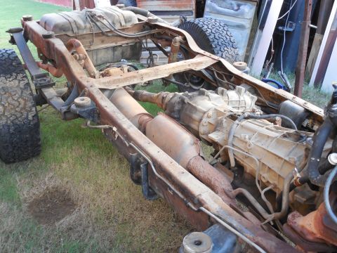 1993 Ford Bronco - Bare rusty boxed frame of a 4x4 truck sitting on grass with the body removed, exposing the automatic transmission and transfer case, drives…