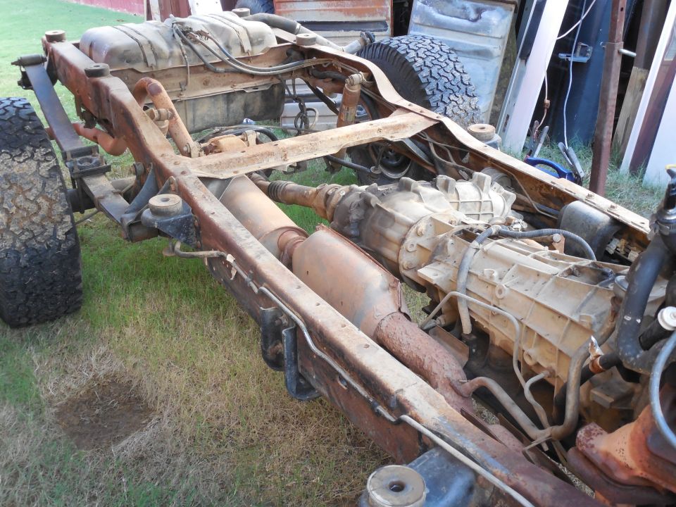 Rusty 4x4 truck frame with body removed showing transmission, transfer case and exhaust