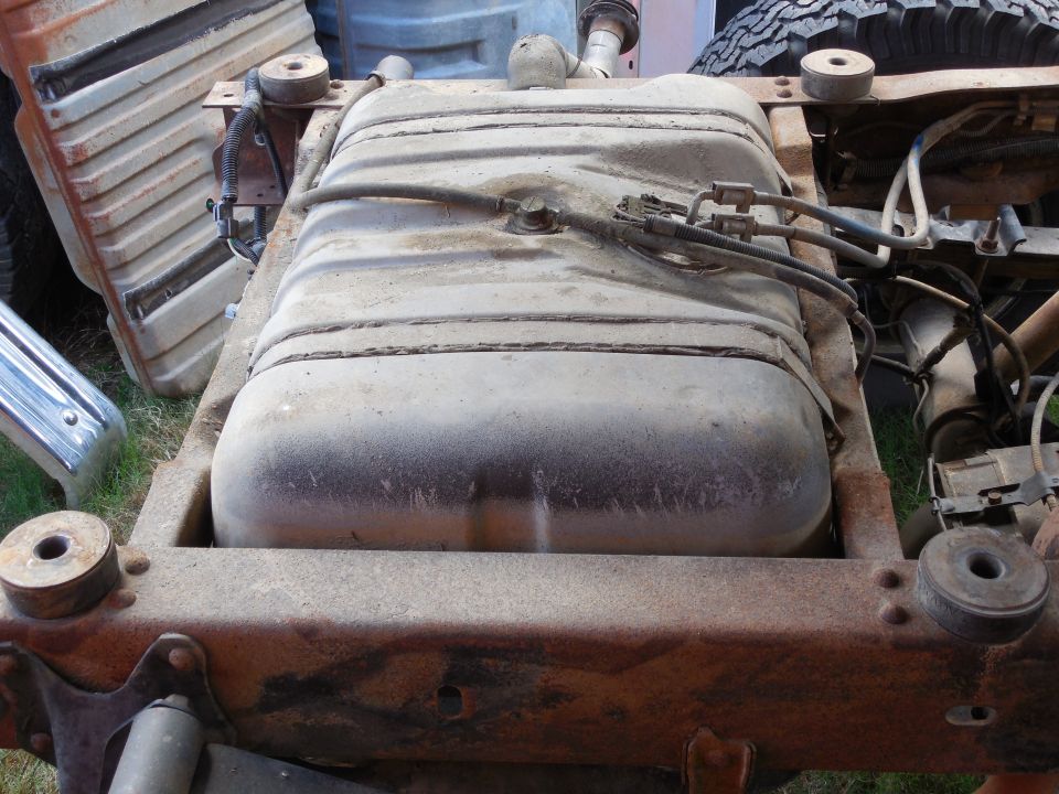 Steel fuel tank strapped inside rusty truck frame rails with body removed, fuel lines on top
