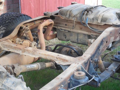 1993 Ford Bronco - Surface-rusted truck frame rail photographed from above with the body removed, showing new black body-mount bushings capped on the frame pe…