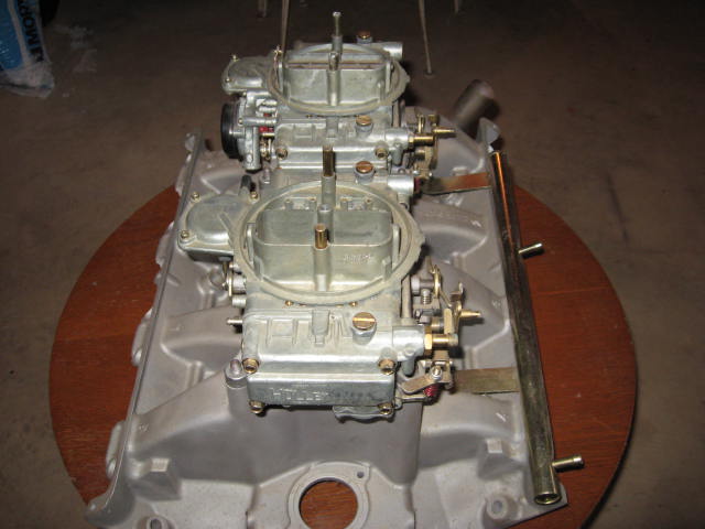 dual Holley carburetors mounted on an aluminum intake manifold, sitting on a round wooden surface