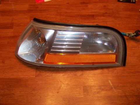 1995 Mercury Grand Marquis - This is a car headlight assembly with an amber turn signal section, photographed on a wooden surface.