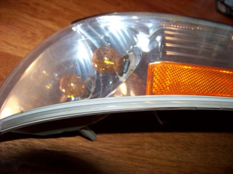 1995 Mercury Grand Marquis - A single headlight assembly is shown, detached from a vehicle, resting on a wooden surface.