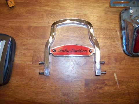 1995 Mercury Grand Marquis - A chrome luggage rack component with a red Harley-Davidson emblem is shown on a wooden surface.