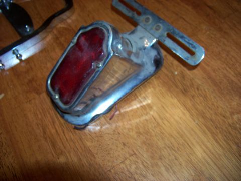 1995 Mercury Grand Marquis - A chrome tail light assembly with a red lens and an adjustable metal bracket is shown on a wooden surface.
