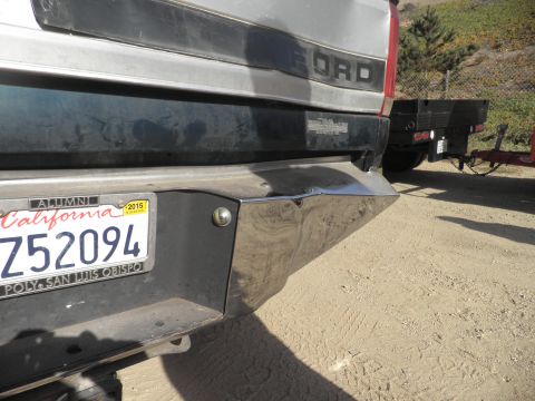 1994 Ford F-250 - Rear view of a silver Ford truck with a dented chrome bumper, hitched to a flatbed trailer.
