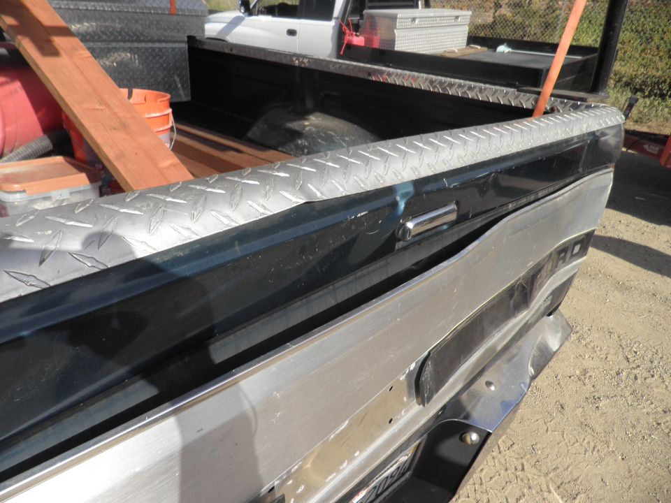 Rear view of a truck bed with diamond plate trim and tools; another truck is visible behind it