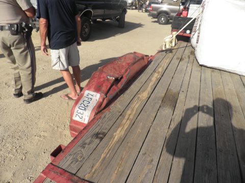 1994 Ford F-250 - A damaged red bumper with a license plate is loaded onto a trailer, with other vehicles and people visible.