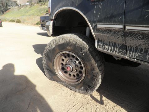 1994 Ford F-250 - A flat tire is visible on a dark truck, with another vehicle in the background.