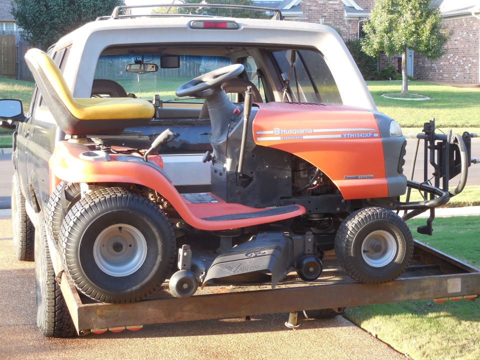 Orange Husqvarna riding lawn mower loaded on a trailer behind a pickup