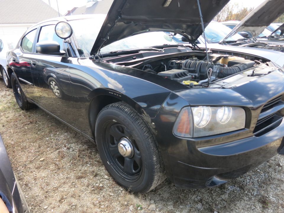 Black police car, hood open, showing engine. Another car is visible behind it