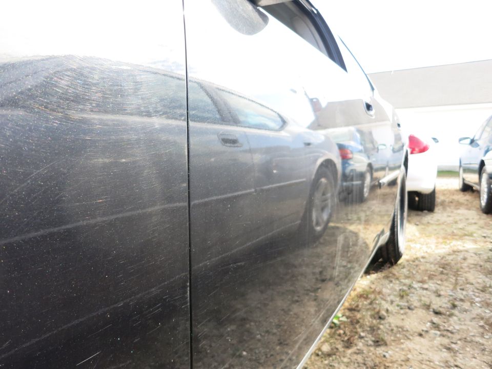 Reflection of a dark sedan on a dirty car door, showing scratches and dust
