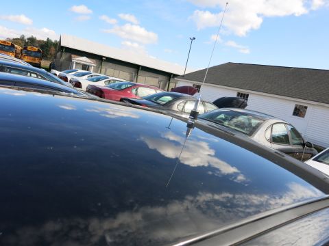 1991 Ford LTD Crown Victoria - A view of parked cars and school buses under a cloudy sky, with the foreground dominated by the reflection on a black car's roof.