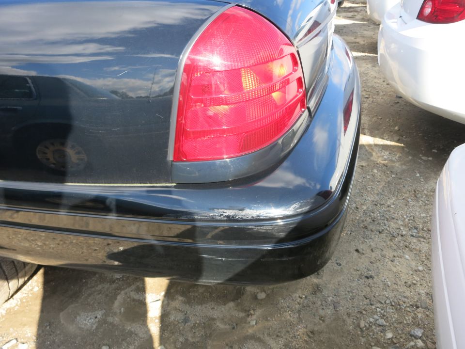 Rear quarter panel, taillight, and bumper of a dark 2003 Ford Crown Victoria. Scratches on bumper