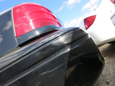 1991 Ford LTD Crown Victoria - Scratches mar the black car's rear bumper and taillight, with a white car visible behind.