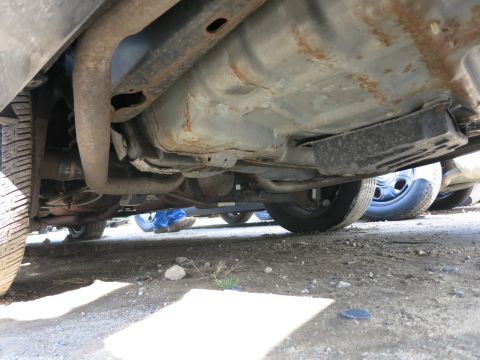 1991 Ford LTD Crown Victoria - A low-angle view of the undercarriage of a vehicle, with other cars partially visible in the background.
