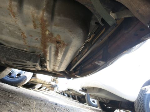 1991 Ford LTD Crown Victoria - The underside of a vehicle shows significant rust on the fuel tank and chassis, with multiple other cars parked nearby.