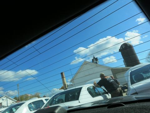 1991 Ford LTD Crown Victoria - A person leans on a white sedan in a parking lot with buildings and a silo in the background.