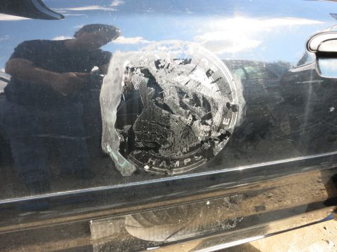 1991 Ford LTD Crown Victoria - A person is reflected in the black paint of a car door, which has a damaged emblem.