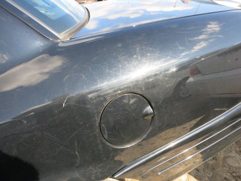 1991 Ford LTD Crown Victoria - Scratched black car body panel showing a fuel door and chrome trim. Another vehicle is visible in reflection.