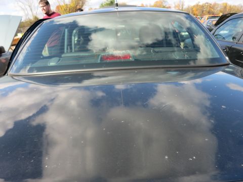 1991 Ford LTD Crown Victoria - The rear of a black sedan is visible, with reflections of clouds on its surface.