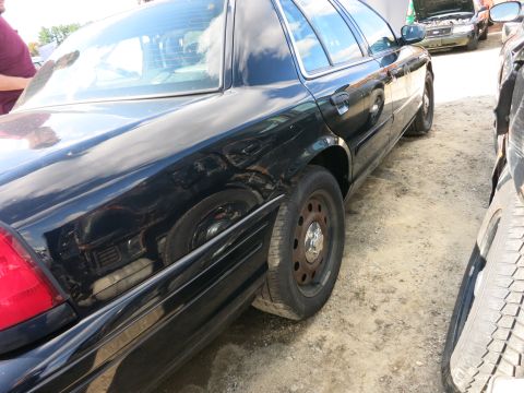 1991 Ford LTD Crown Victoria - A black sedan is parked on a dirt lot next to another vehicle, with its hood open.