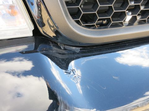 1991 Ford LTD Crown Victoria - Close-up of a damaged black car bumper and grille, showing reflections of the sky.