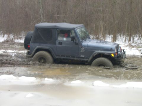 1995 Ford Bronco - Jeep Wrangler is stuck in a muddy, watery trail with snow on the ground.