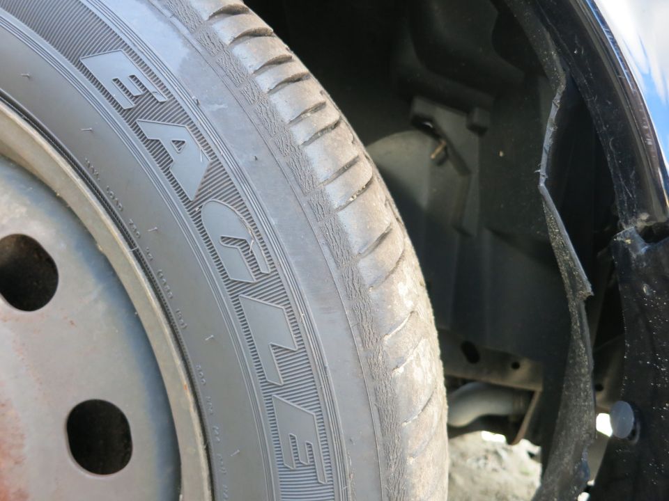 Close-up of a car's front tire and wheel well. The tire has some text on it