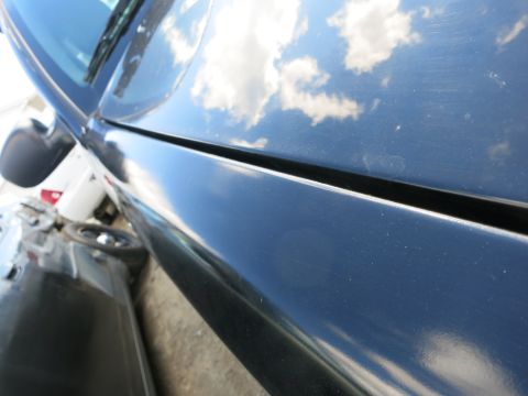 1991 Ford LTD Crown Victoria - Close-up of a dark blue car's side panel, showing reflections of clouds and another vehicle.