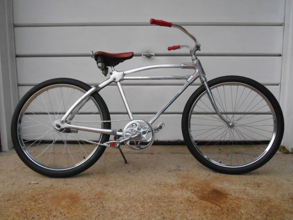 Chrome cruiser bicycle with red grips and a brown leather seat, parked in front of a garage door