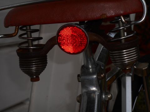 Red bicycle saddle with chrome springs and a red reflector on the seat post