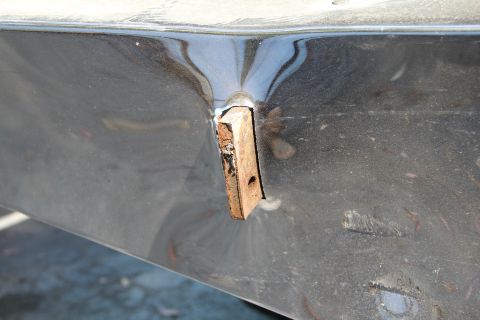 1994 Ford F-250 - A close-up view of a damaged vehicle body panel with a piece of wood inserted into a hole.
