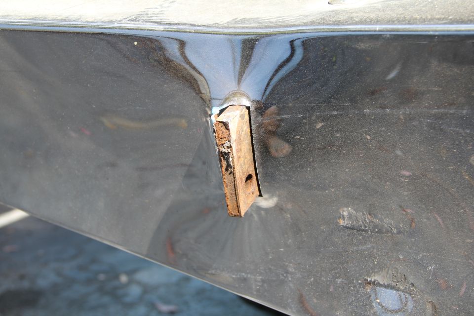 Close-up of a dark-colored vehicle body panel with a wooden block inserted into a hole