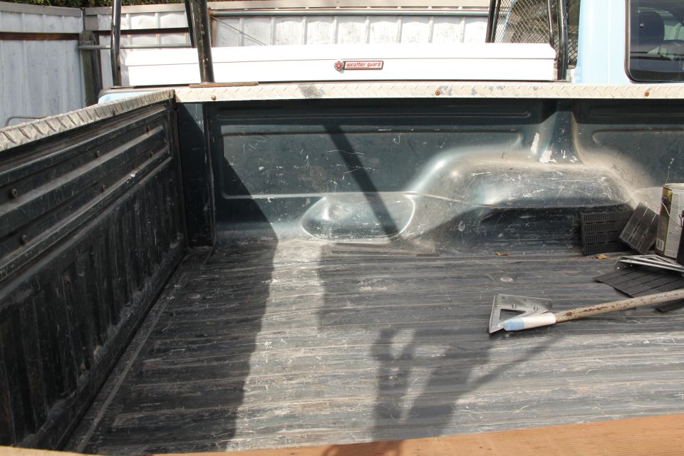 Truck bed with a toolbox and ladder rack, showing wear and tear. A shovel rests inside