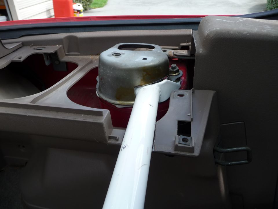 Interior view of a car's dashboard area showing a metal strut bar attached to a silver component
