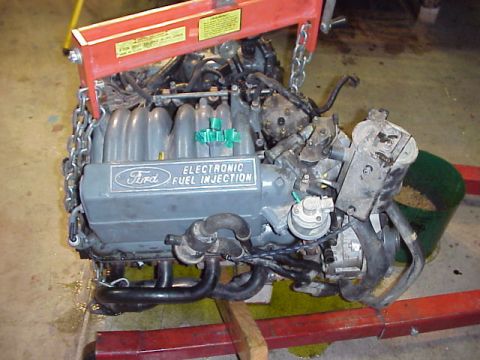 1989 Ford Bronco - Engine labeled "Ford ELECTRONIC FUEL INJECTION" is hoisted for repair or rebuild.