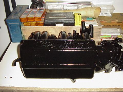 1989 Ford Bronco - Black painted Ford engine valve cover with various automotive parts and supplies in the background.