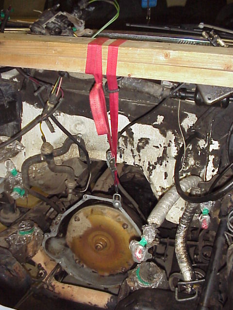 1989 Ford Bronco - Engine transmission connection with bell housing removed, held by a support beam and straps.