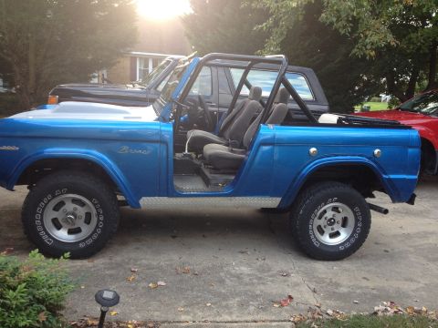 1974 Ford Bronco - A blue Ford Bronco is parked in a driveway with its doors off and a roll cage installed.