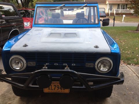 1974 Ford Bronco - A blue 1974 Ford Bronco is seen from the front, parked next to other vehicles.