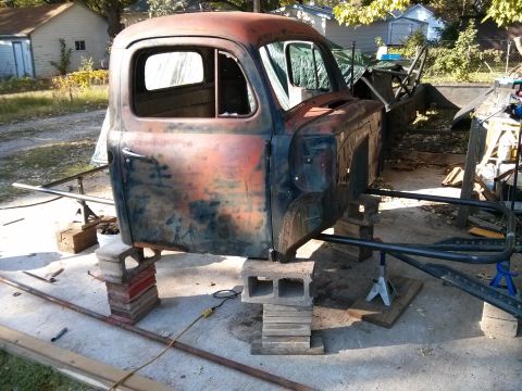 1986 Ford Bronco - A weathered truck cab sits on a makeshift support structure of cinder blocks and wood.
