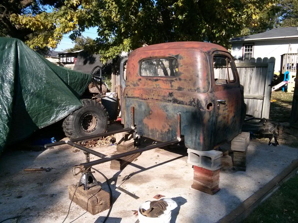 rusted truck cab on cinder blocks with tarp-covered object to the left